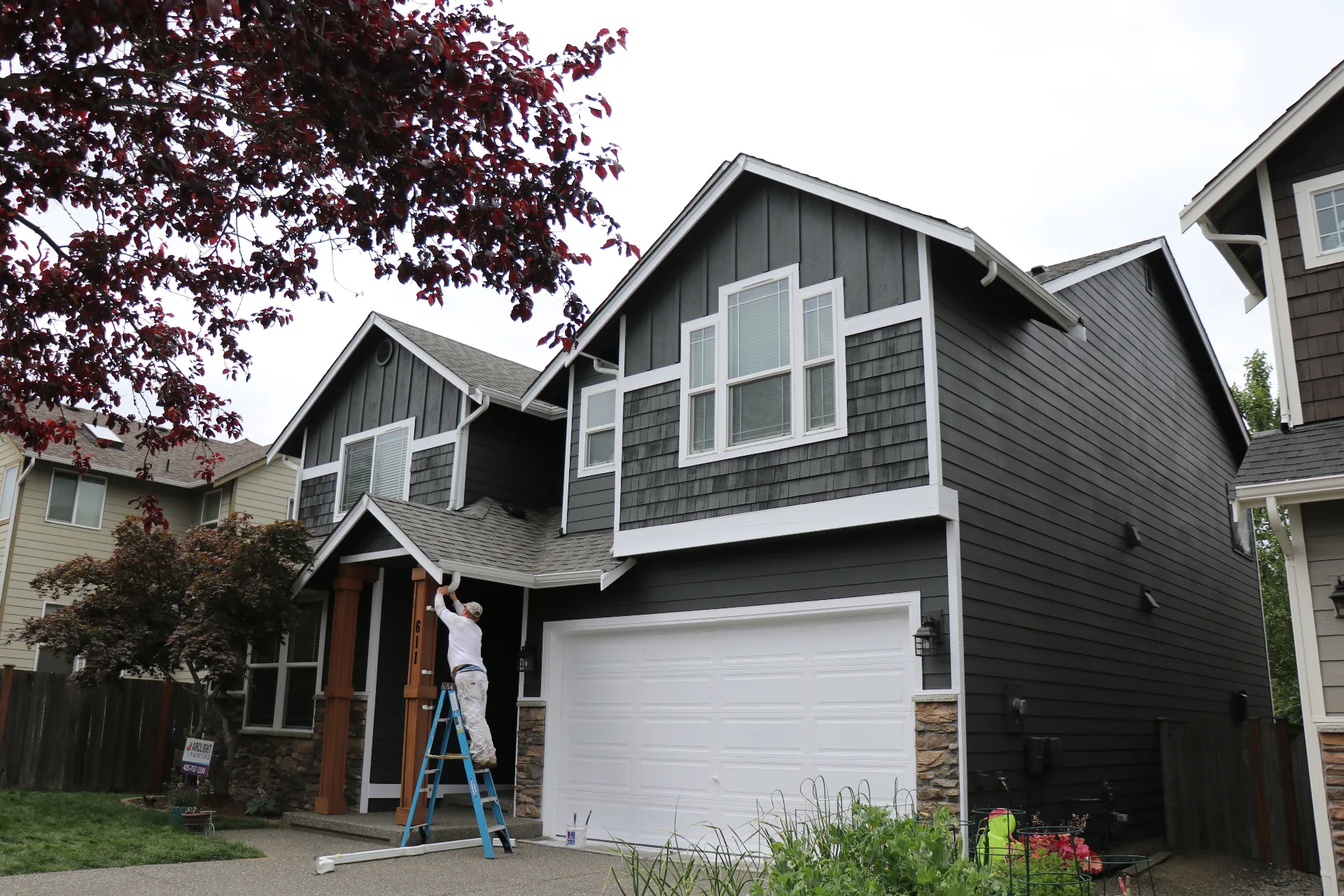 Arclight painter on ladder painting dark exterior trim in Bothell